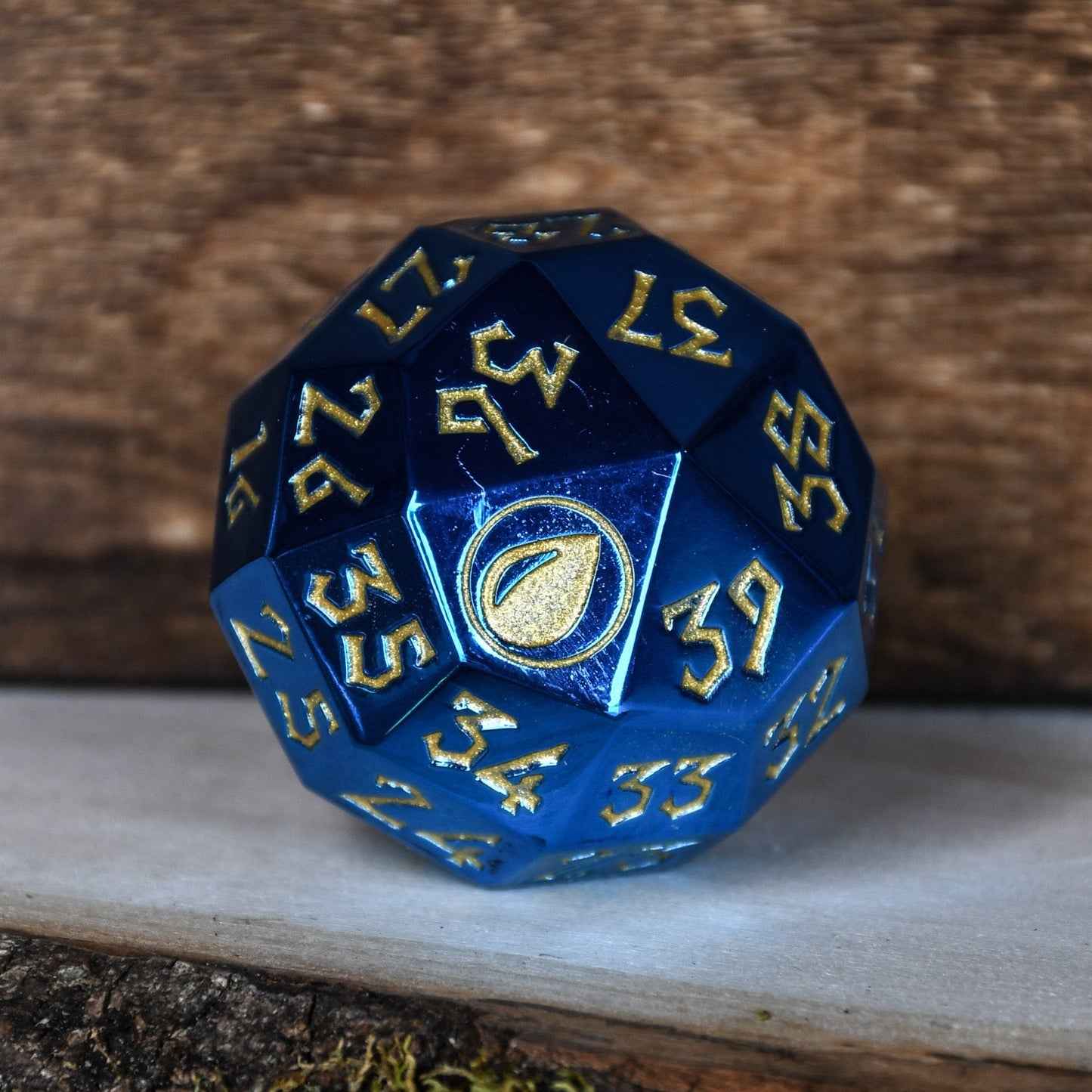 A solid-metal spindown life counter dice, with blue coloring and gold numbers, displayed on a wooden surface for magic the gathering