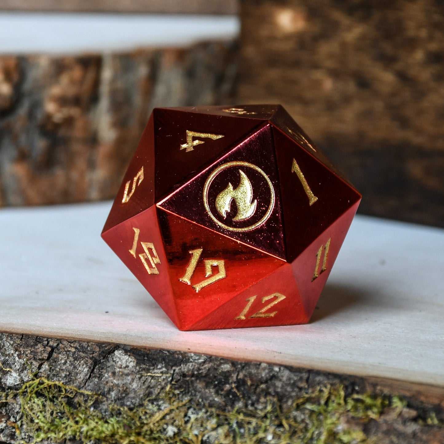 A red and gold metal D20 dice with numbers and a symbol on each face, placed on a wooden surface with moss at the bottom.