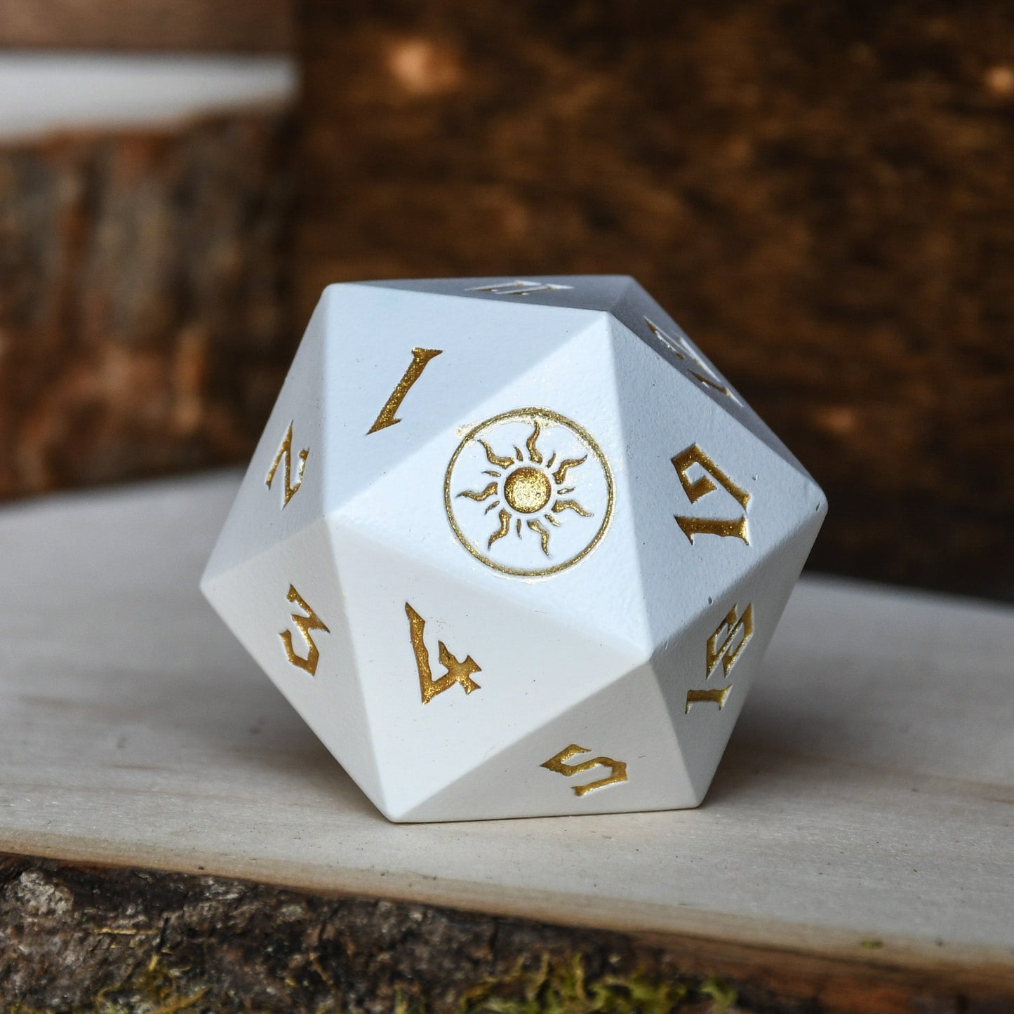 A white-colored metal D20 dice with gold numbers and symbols, used as a spindown life counter for trading card games, displayed on a wooden surface.