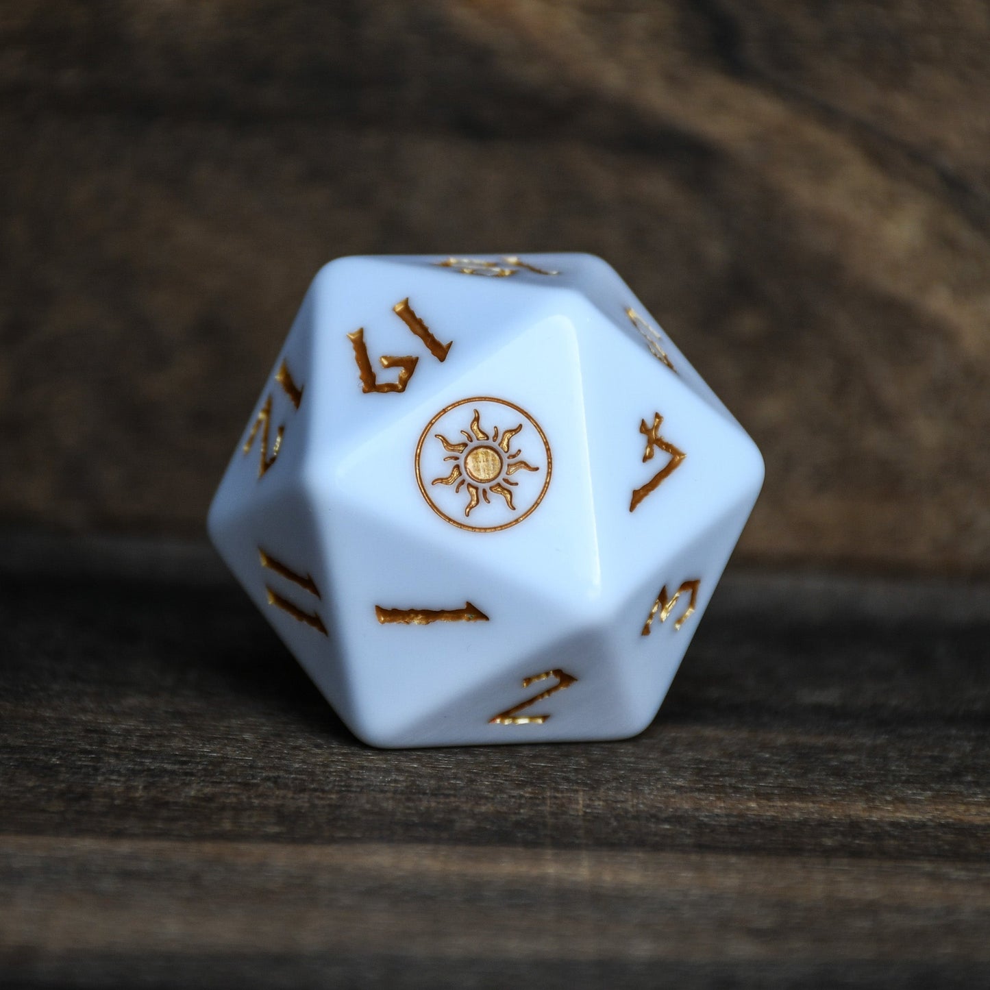 White polyhedral dice with gold numbers and symbols on a wooden surface