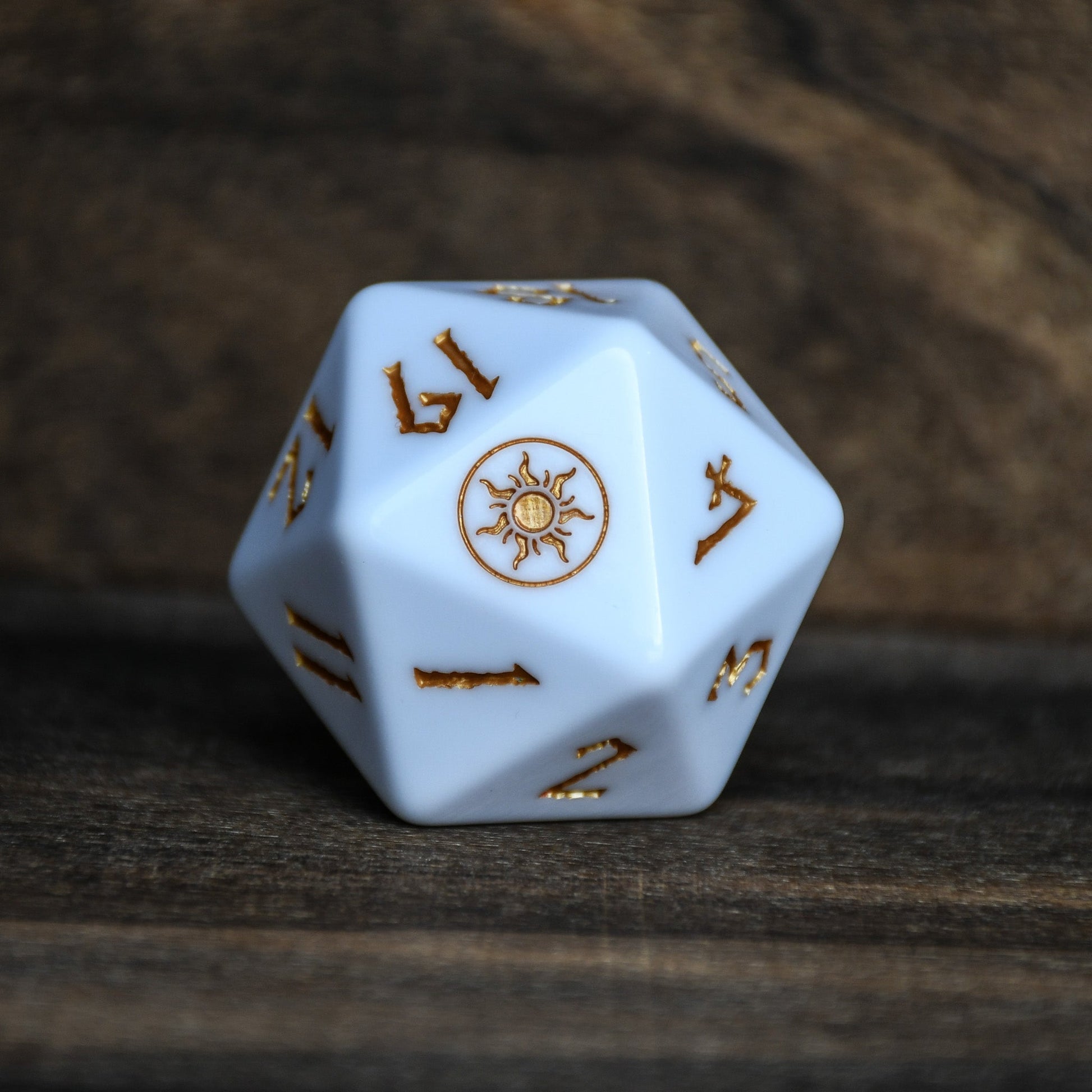 White polyhedral dice with gold numbers and symbols on a wooden surface