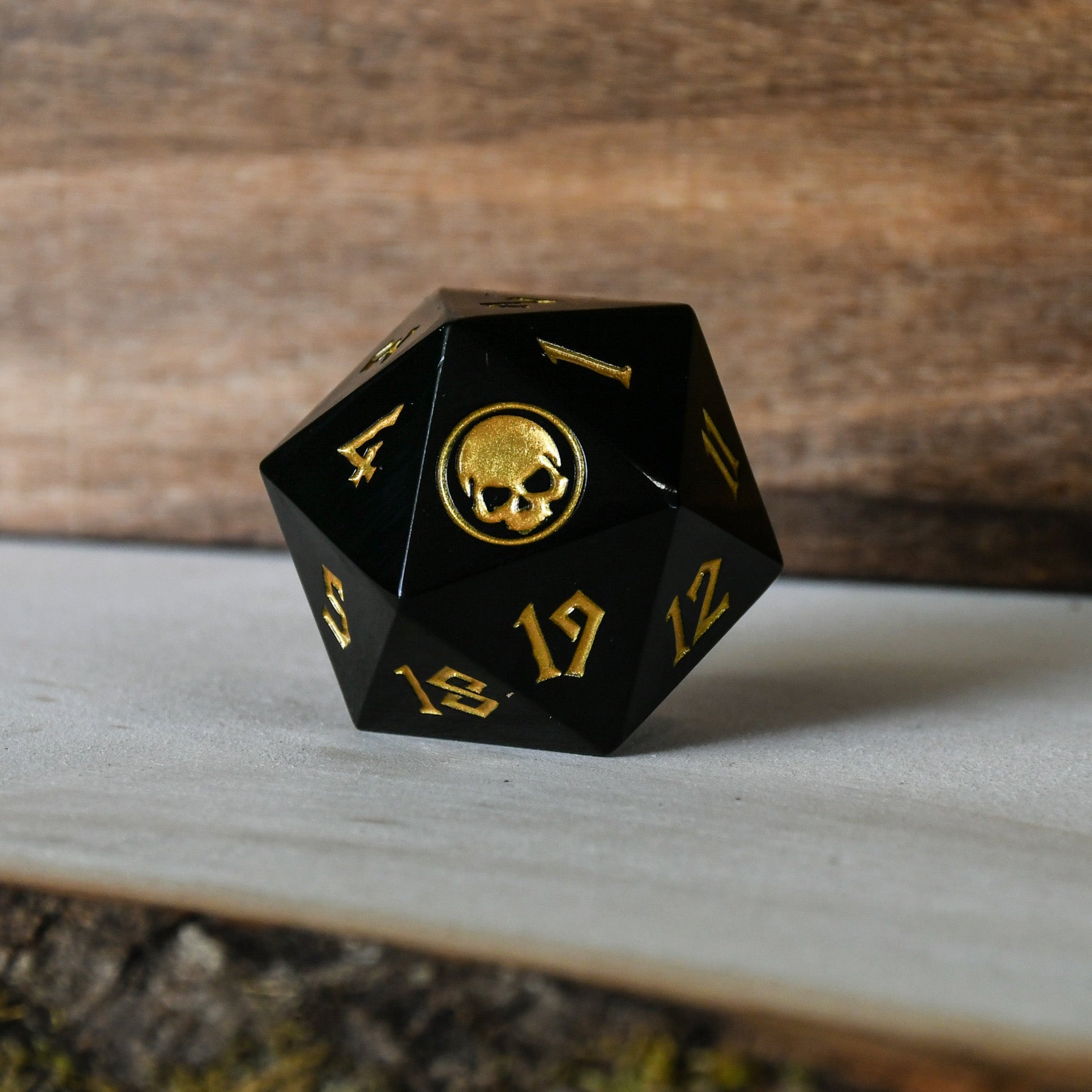 An oversized solid-metal spindown life counter dice with black color and gold numbers, placed on a wooden surface.