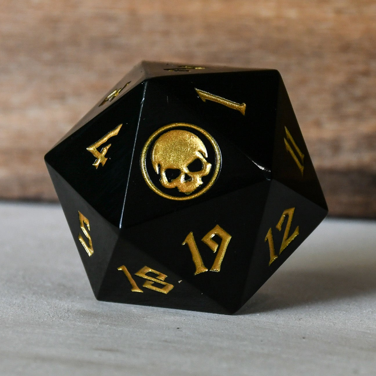 Black polyhedral dice with gold numbers and a skull design on a wooden background